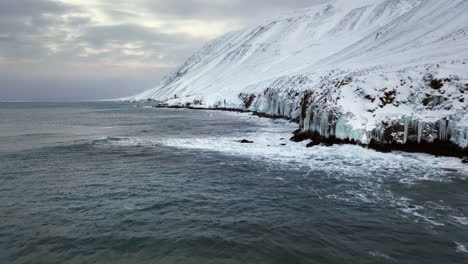 Wellen-Rollen-Gegen-Die-Steilen-Gefrorenen-Bergwände-In-Der-Weißen-Winterlandschaft-Von-Island