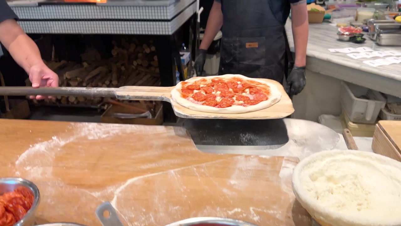 Chef professionista con grembiule nero inforna una pizza ai peperoni in un tradizionale forno a legna a Bangkok