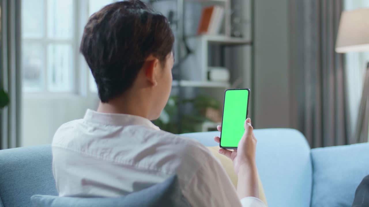 Man Watching Smartphone With Green Screen While Lying On Sofa In The Living Room