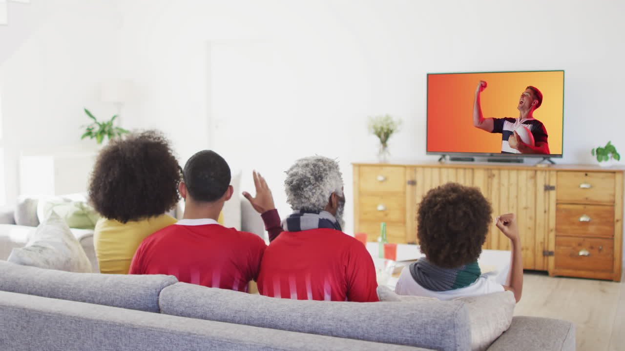 Famiglia birazziale che guarda la TV con un giocatore di rugby maschio caucasico con la palla sullo schermo.