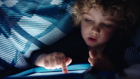 Un-Niño-Feliz-Usando-Una-Tableta-Digital-Bajo-Una-Manta-Disfrutando-Aprendiendo-Con-Tecnología-De-Pantalla-Táctil-Jugando-Juegos-Divirtiéndose-A-La-Hora-De-Dormir