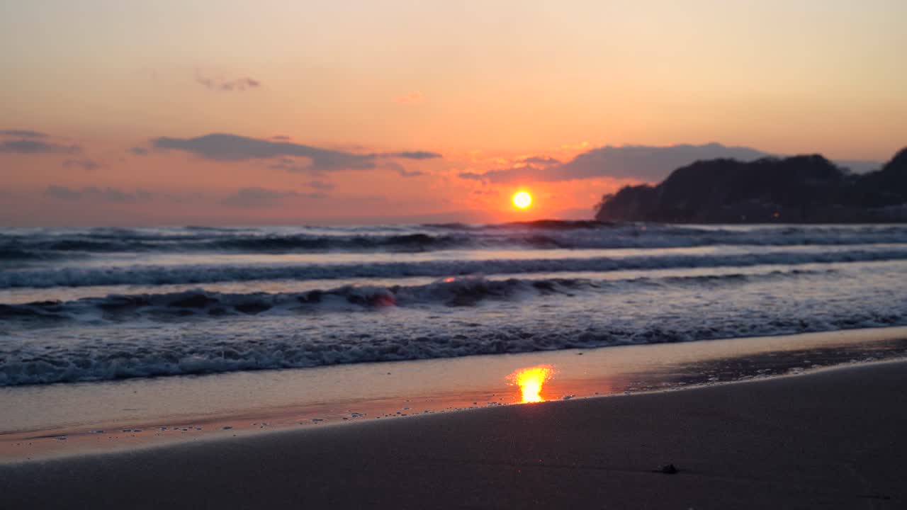 Beautiful sunset at beach, silhouette clouds and island in the distance - low angle locked off shot