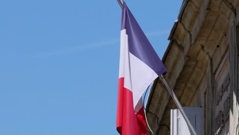 a close-up of the french flag waving on a historic stone building under a clear blue sky.