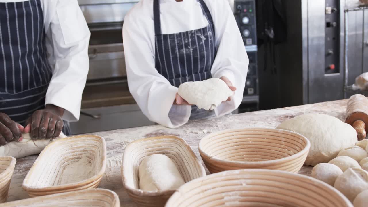 Midsection of diverse bakers working in bakery kitchen, forming bread form dough, slow motion