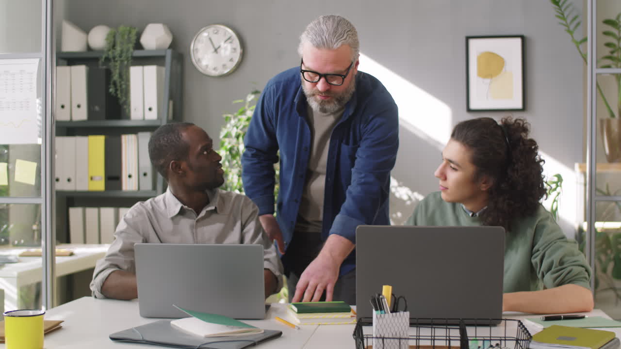 mentor sénior que enseña a jóvenes aprendices multiétnicos en la oficina