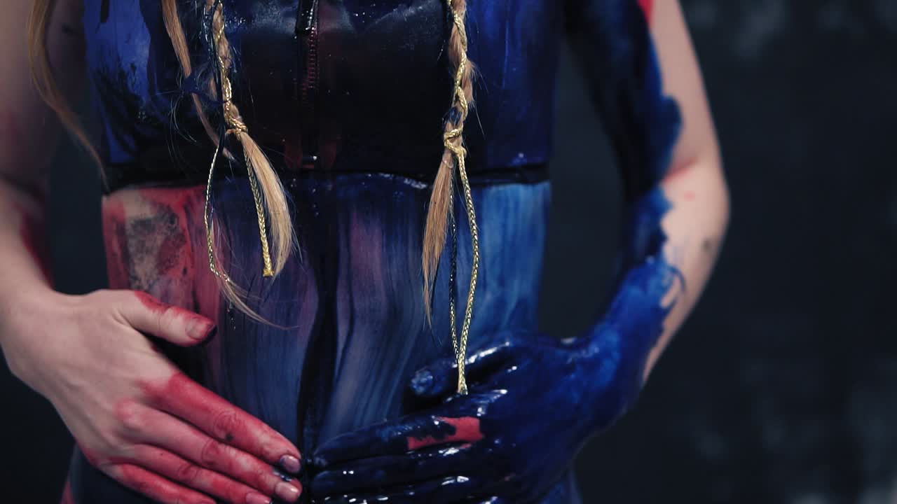 Seductive girl with a beautiful body smears paint on her belly. Close up. Black background