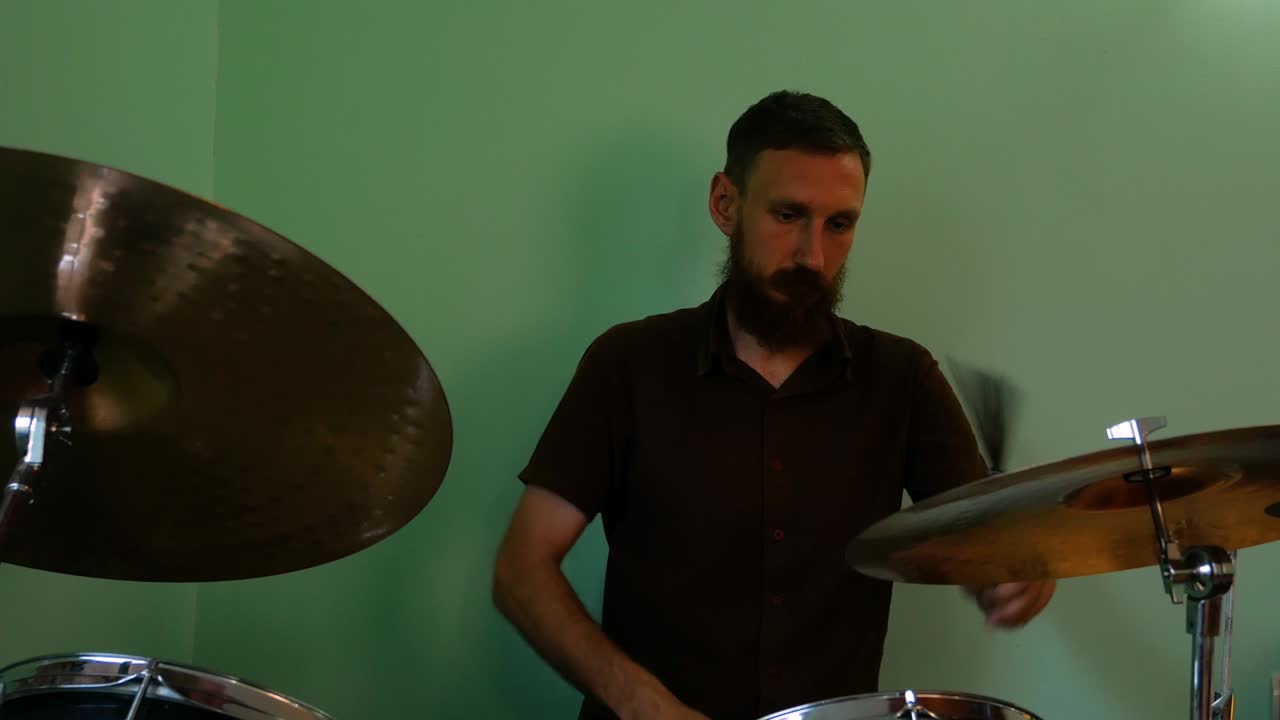 baterista calentándose con pinceles de batería. hombre barbudo tocando música rock y metal en la batería en el fondo de la pared verde. ensayo de la banda de música atascando imágenes de 4k.
