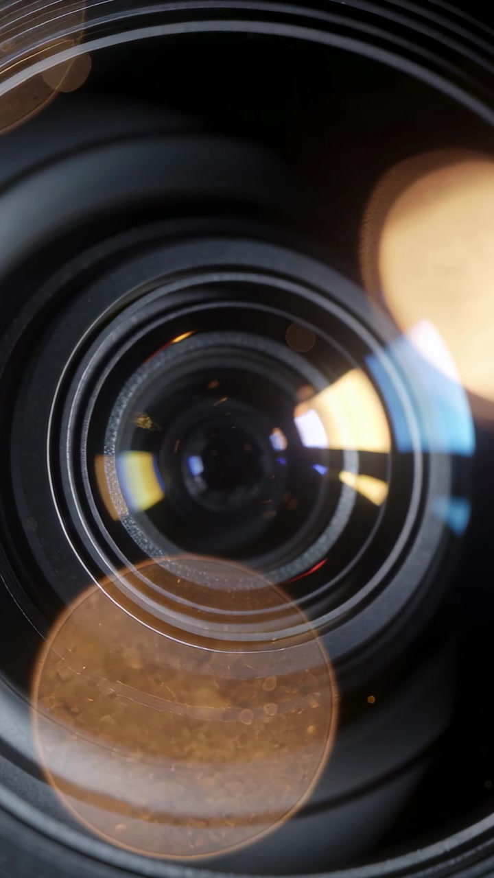 Video verticale: Luci che si muovono rivelano gli anelli dell'obiettivo della fotocamera e l'apertura in uno studio in penombra, con effetto bokeh.