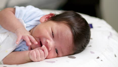 panning from the right to the left on a newborn baby lying on its crib as it is blinking its eyes and while it is dozing off to sleep