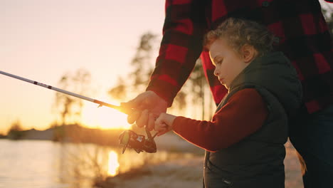 curious little boy is learning to catch fish by fishing rod father or grandpa is helping