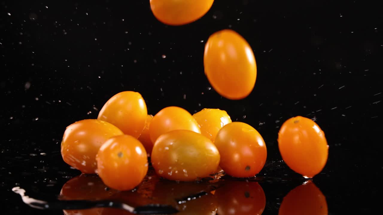 Cherry tomatoes fall and splash on a reflective black surface, creating dynamic motion and vibrant contrast