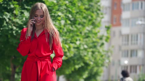 gorgeous young lady with mobile phone. beautiful woman with long hair talking on the phone happily. pretty girl standing near the green tree. slow motion.