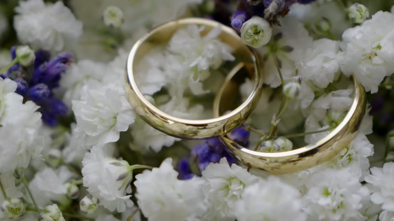 Golden wedding rings lying on a bouquet of white and purple flowers