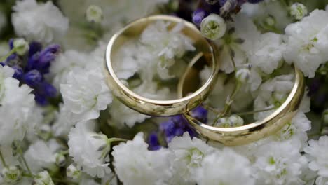 golden wedding rings lying on a bouquet of white and purple flowers