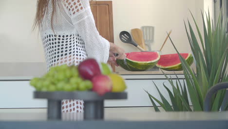 in the kitchen, a sexy woman slices a watermelon with a large knife in slow motion