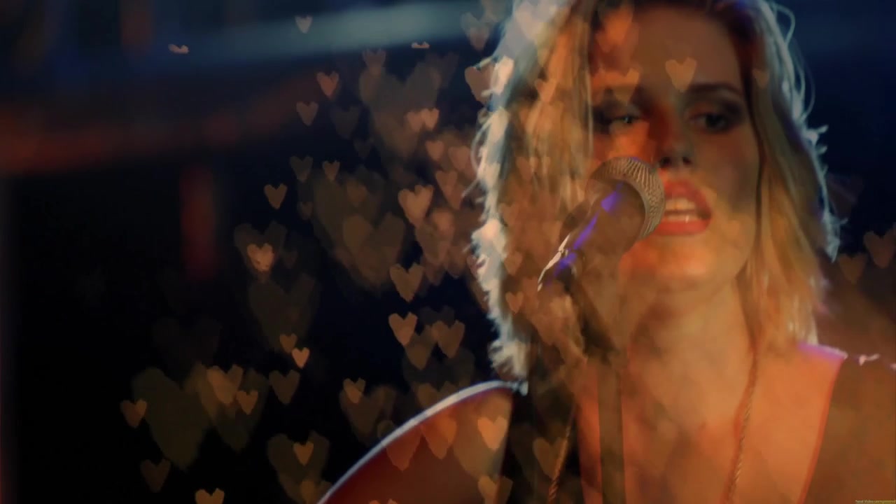 Musicista donna che regola la tracolla e strimpella accordi mentre si esibisce al microfono con effetto bokeh a forma di cuore