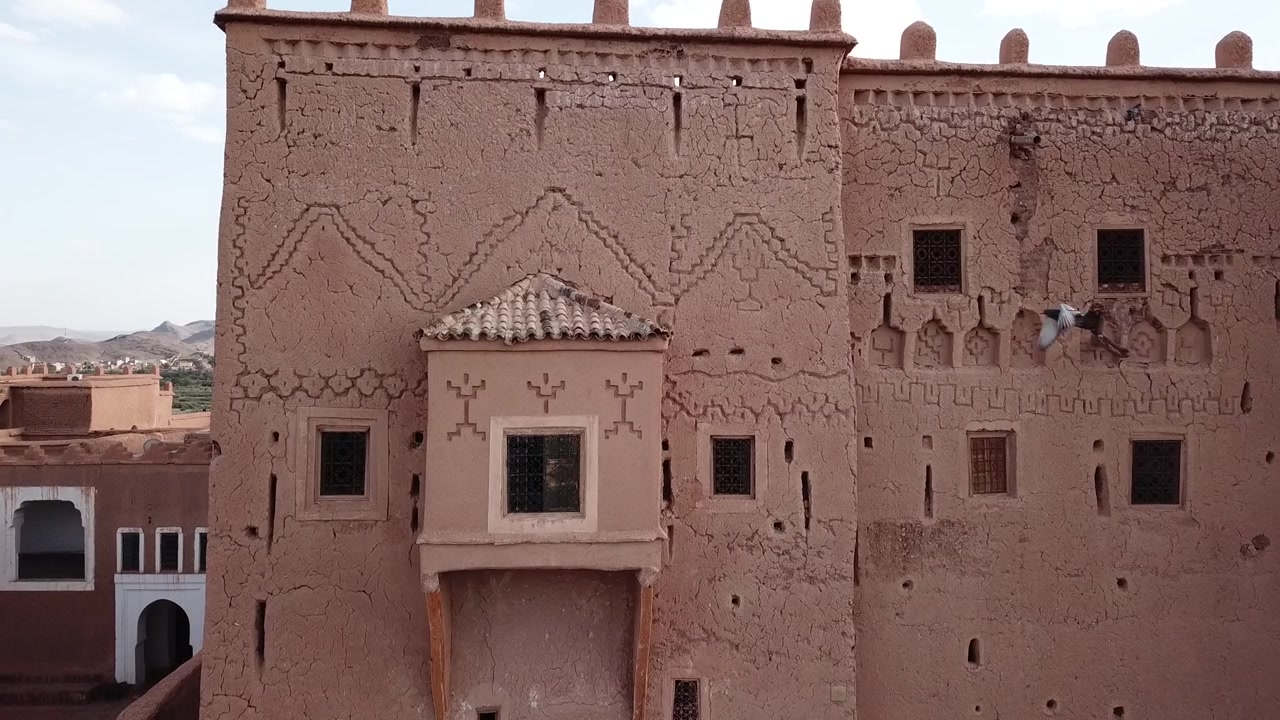 Zoom lento del drone sulla facciata storica della Kasbah di Taourirt a Ouarzazate, che rivela la distintiva architettura in terra cruda e il patrimonio culturale del Marocco meridionale