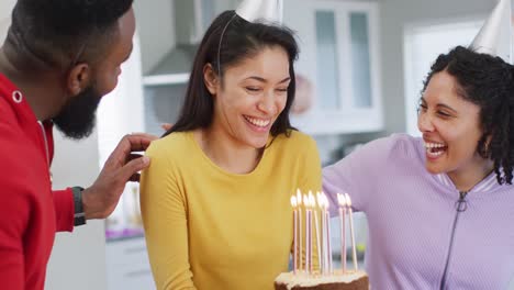 happy biracial woman holding birthday cake celebrating birthday with diverse friends, in slow motion