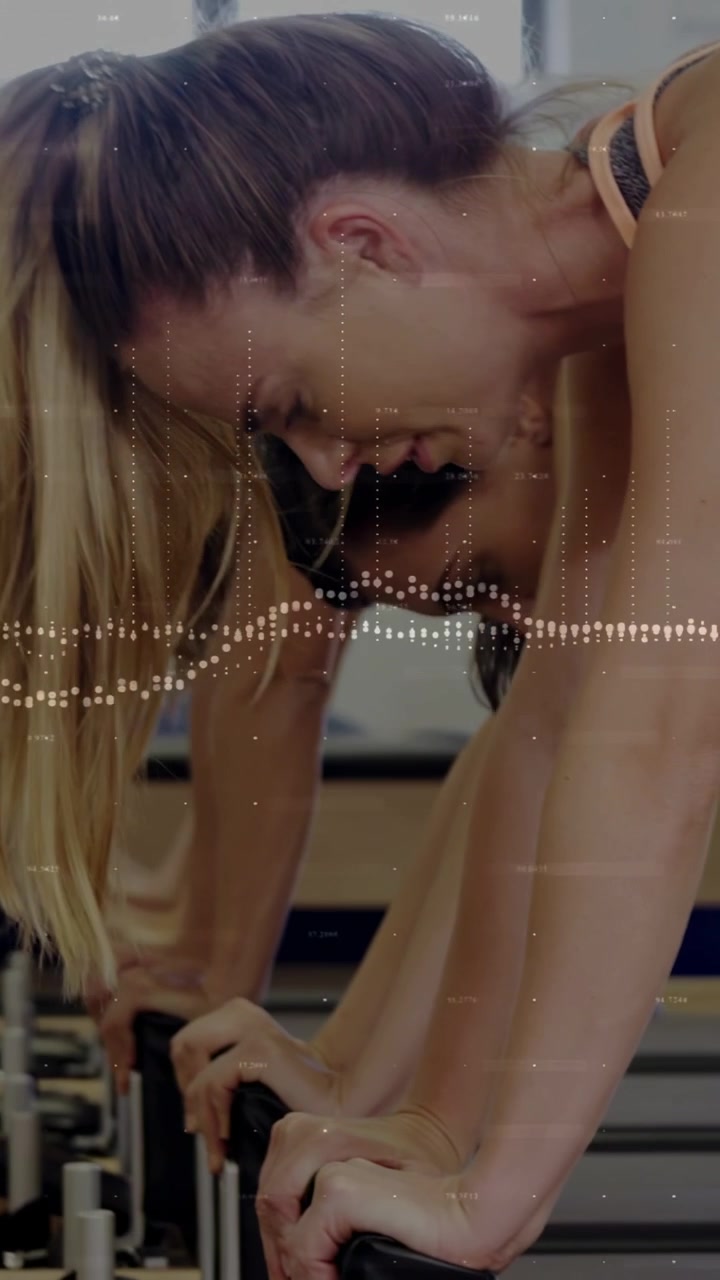 Video verticale: Donna in prima fila che fa pilates premendo una barra, passando alle maniglie, eseguendo movimenti a impulsi, tonificando.