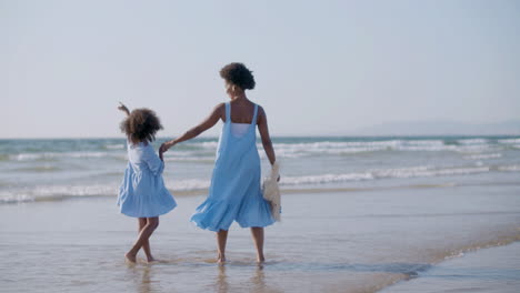 woman walking along seashore with daughter, holding hands and enjoying the view