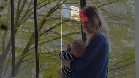 holding baby near large window, woman watching trees with animation outside