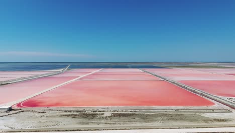 Fliegen-über-Der-Albanischen-Meersalzfarm-Mit-Rosafarbenem-Sediment-Und-Blauem-Himmel-Am-Meer