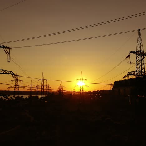 transmission lines at sunset. high-voltage electric towers near the industrial factory with smoking pipes in the evening. motion camera top down.