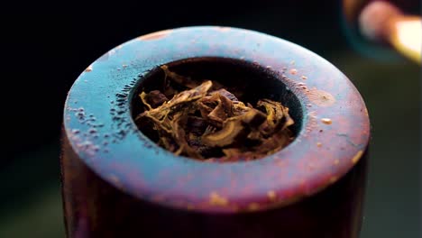 fresh dry brown tobacco filled inside a pipe hole burned by wooden match close up of smoking and producing smoke vintage style of inhaling nicotine multiple colours set on the dark background cinema