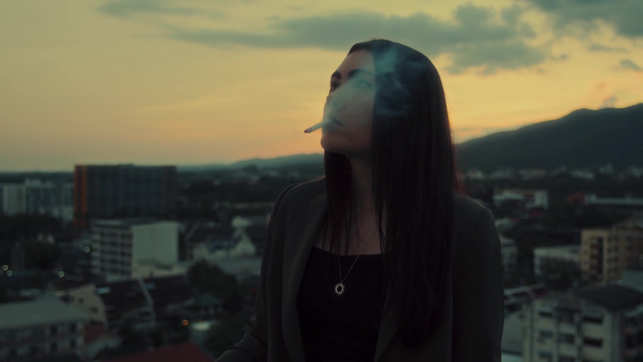 Giovane donna che fuma una sigaretta sul tetto al tramonto