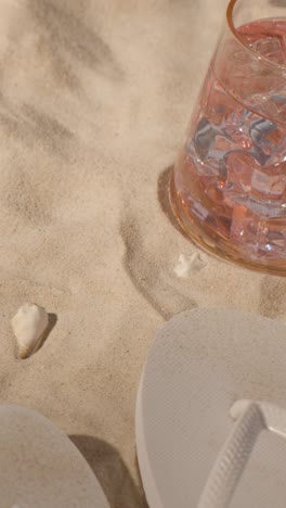 Vertical-Video-Summer-Holiday-Concept-Of-Sunglasses-Sun-Hat-Flip-Flops-And-Cold-Drink-On-Beach-Towel-On-Sand