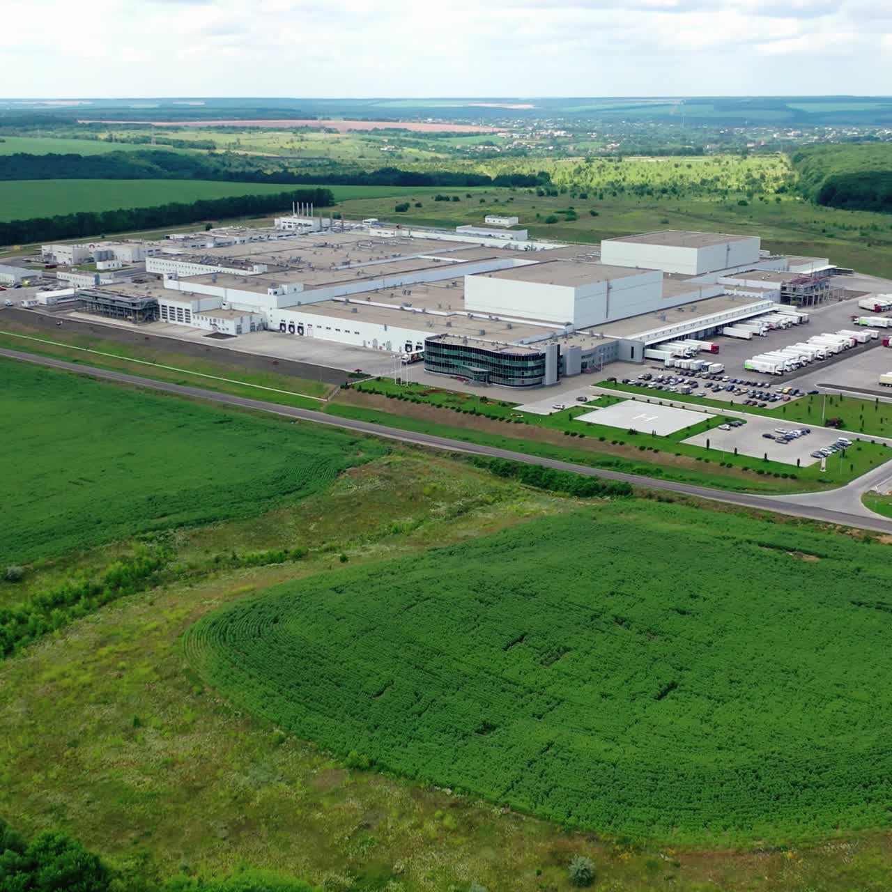 Huge industrial plant surrounded by green nature. Modern complex of agricultural factory among fields in summer. Aerial view