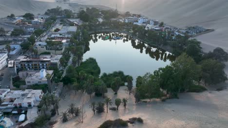 Desert-oasis-Huacachina,-Peru-with-lake-and-palms,-with-great-sand-dunes-in-the-background