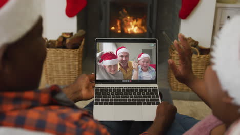 african american couple with santa hats using laptop for christmas video call with family on screen