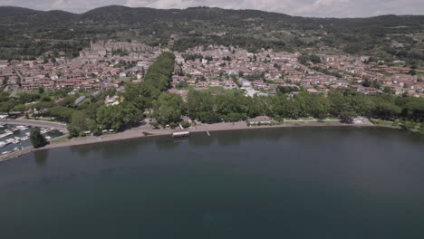 Drohnenschuss,-Der-An-Einem-Sonnigen-Tag-über-Den-Bolsenasee-In-Italien-Fliegt-Und-Vom-Wasser-In-Die-Alte-Mittelalterliche-Stadt-Mit-Einer-Burg-Und-Alten-Gebäuden-Auf-Dem-Hügel-Kommt