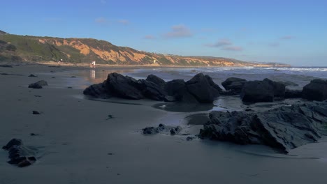 Playa-Corona-Del-Mar-Con-Vista-Estática-De-Las-Rocas-Con-Acantilados-Y-Pequeñas-Olas-Del-Océano-Pacífico-En-La-Parte-De-Atrás