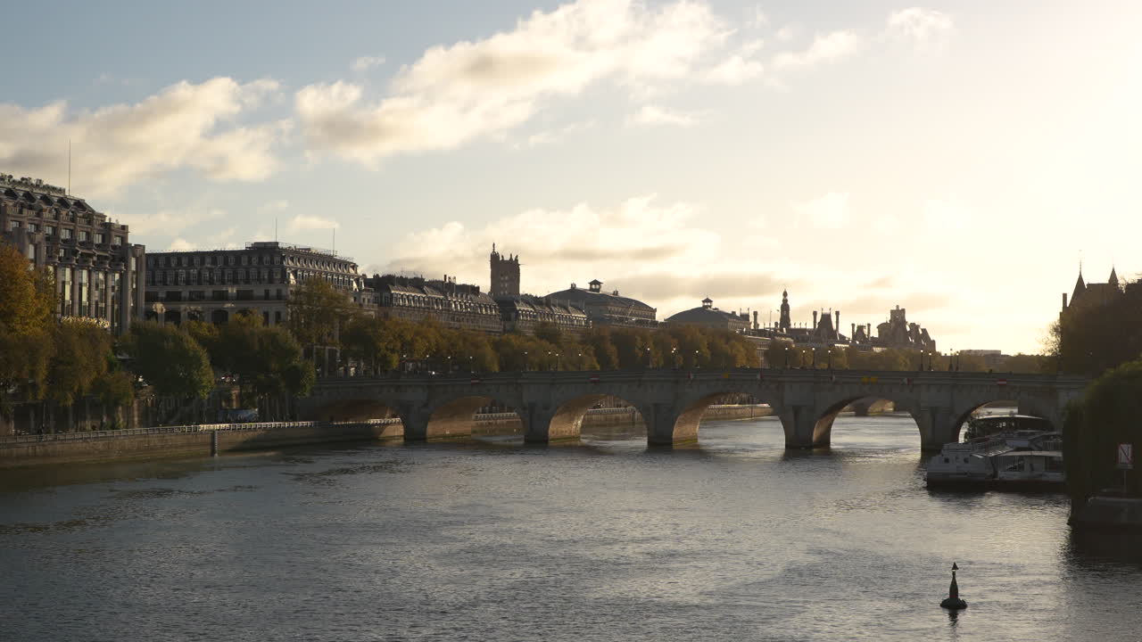 Golden-hour view of the Pont Neuf bridge over the Seine River in Paris with warm sunlight, historic buildings, and boats along the riverbank