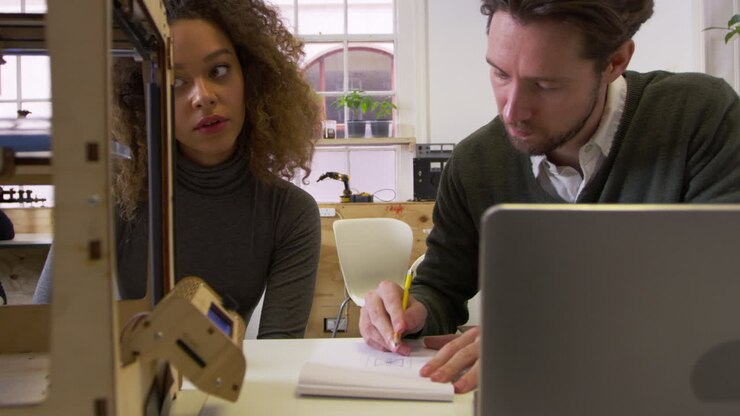Two designers working in a design studio watch a 3D printer, shot on R3D