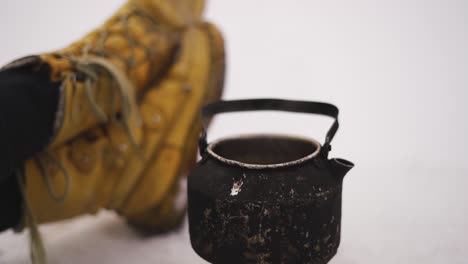 steaming pot in the snow and hiker boots lying on the ground. winter trip. hot drink outdoors.