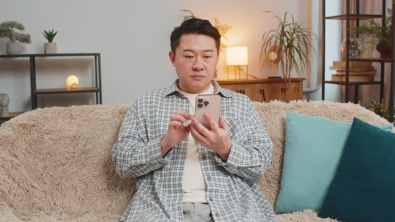 Asian middleaged man at home celebrating online game victory shocked by good news on phone