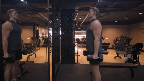 fitness man standing by mirror training shoulders in empty gym