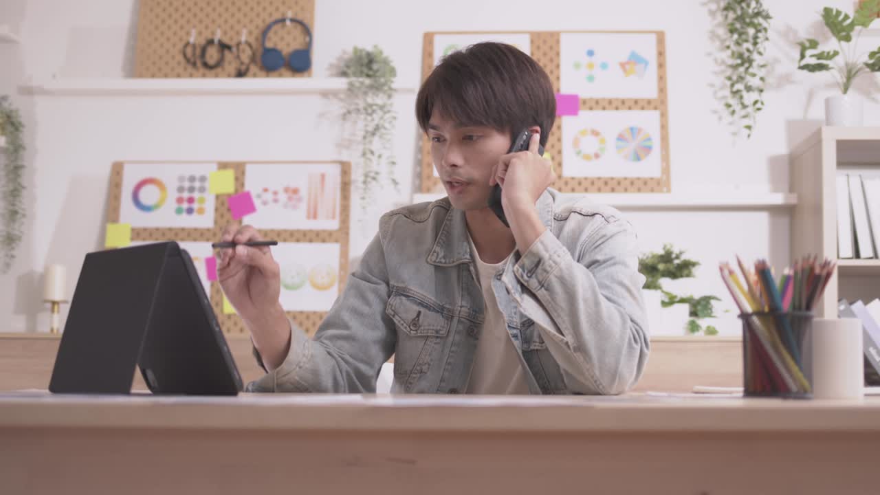 아시아인 디자이너는 스마트폰으로 커뮤니케이션을 하고, 프로젝트와 서류 작업을 하며, 노트북으로 책상에서 집에서 일합니다.