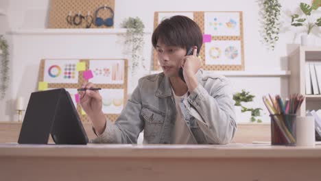 아시아인 디자이너는 스마트폰으로 커뮤니케이션을 하고, 프로젝트와 서류 작업을 하며, 노트북으로 책상에서 집에서 일합니다.