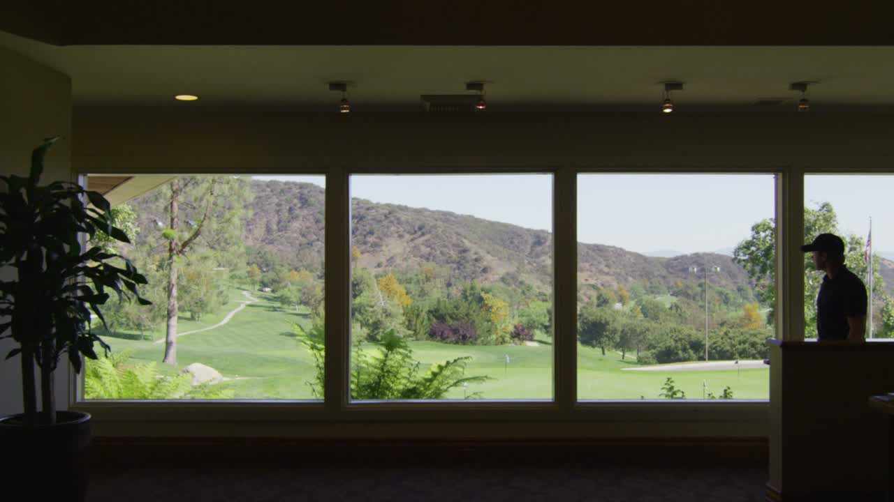 A golfer inside a country club with a golf course visible through the windows