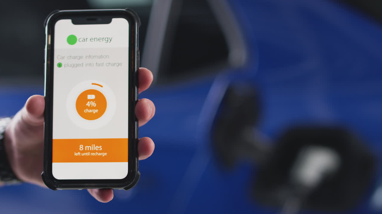 hombre cargando un coche eléctrico con cable usando una aplicación en el teléfono para monitorear el nivel de la batería