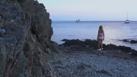 hermosa niña camina hacia el mar y arroja una piedra al agua, y luego observa cómo se hunde