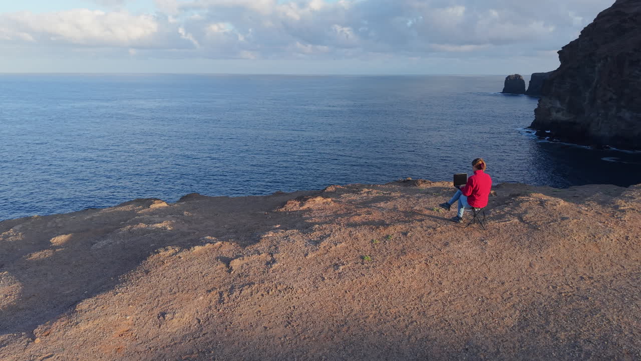 Female freelancer working with her laptop on a cliff with a breathtaking view of the ocean