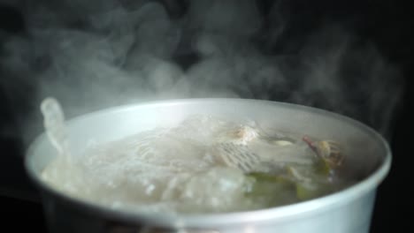 thai food, boiled spicy soup of fish at kitchen with white smoke and steam effect on black background. culture travel and culinary concept.