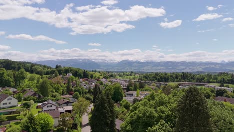 aerial establishing shot of luxury swiss neighborhood with solar panels on homes. snowy peak of alps in distance. rising wide shot. sunny summer day in switzerland.