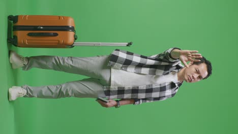 full body of asian male traveler with luggage and passport looking at camera and disapproving with no hand sign in the green screen background studio