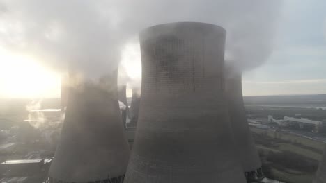 aerial orbit pull back view across uk power station cooling towers smoke steam emissions at sunrise